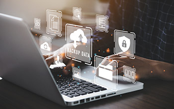 A person typing on a laptop with data backup and security icons hovering over the image.