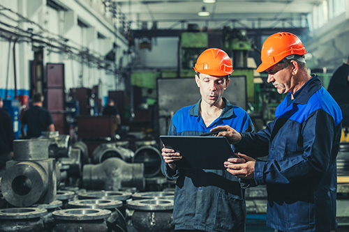 Two workers look at a tablet in a manufacturing facility.